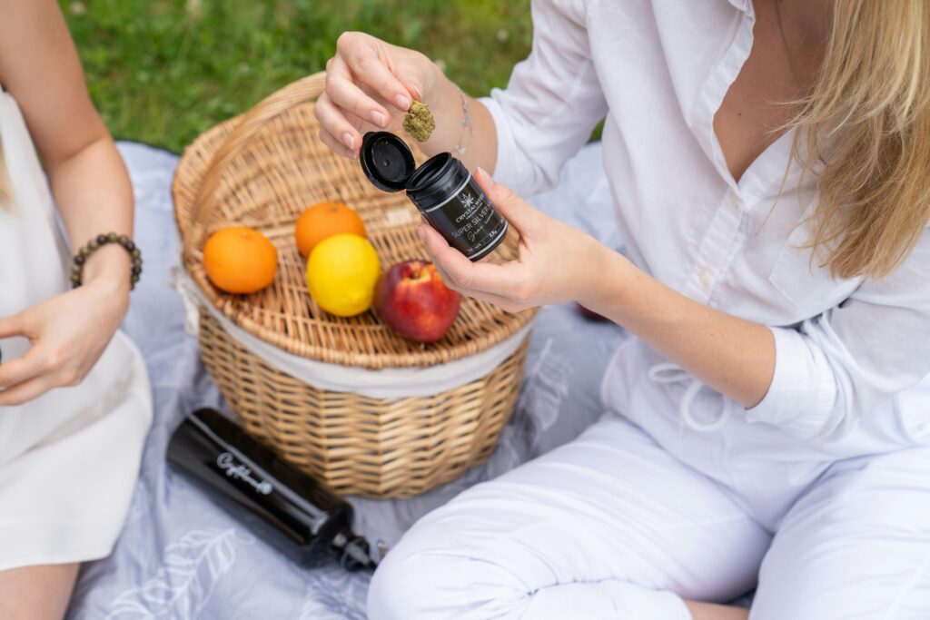two women sitting on the grass with a basket of fruit